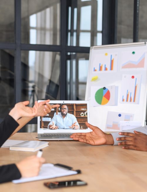 Lively team holds meeting with black boss via video link in modern office, teleconference meeting using laptop, african businessman having video call with his business team online, talk about strategy